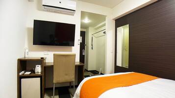 A hotel room with a bed, a desk with a chair, a television, a small refrigerator, and an air conditioning unit.