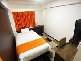 Habitación de hotel con cama, escritorio, silla, televisor y ventana con cortinas.