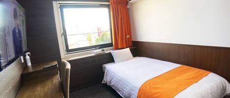 A hotel room with a bed, a desk, a TV, and an air conditioning unit.
