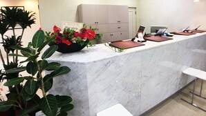 Zona de recepción con mostrador de mármol, un arreglo floral, un reloj y un cartel con texto en japonés.