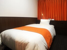 A hotel room with a bed, a nightstand, a window with orange curtains, and a headboard.