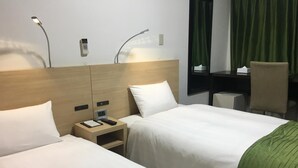 Habitación de hotel con dos camas, un escritorio, una silla y una ventana con cortinas.