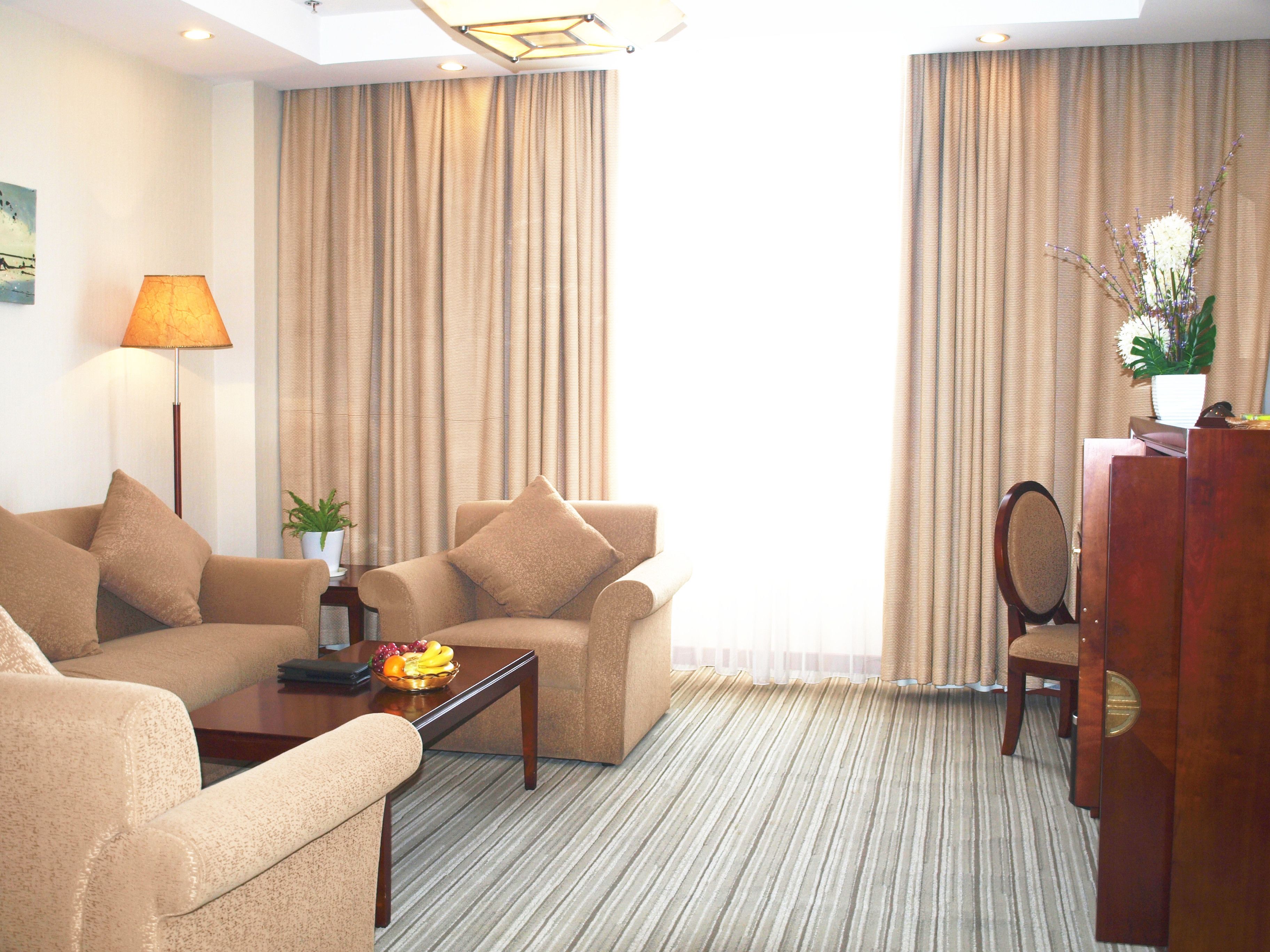 Ein Hotelzimmer mit zwei beigen Sofas, einem Holztisch mit Obst, einem Schreibtisch mit Stuhl und Vorhängen.