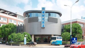 A modern building with a curved facade, a blue sign with white text, and a bus parked in front. - Century Hotel Taicang (Suzhou)