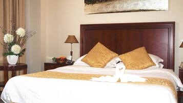 A hotel room with a large bed, two pillows, a nightstand with a lamp, a vase with flowers, and a painting on the wall.