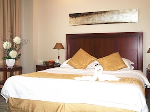 A hotel room with a large bed, two pillows, a nightstand with a lamp, a vase with flowers, and a painting on the wall. - Century Hotel Taicang (Suzhou)