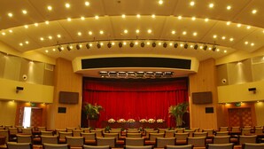 A theater with a red curtain, multiple rows of chairs, and a stage with lighting equipment. - Century Hotel Taicang (Suzhou)