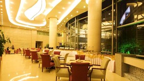 A spacious hotel lobby with a modern design, featuring a large seating area with tables and chairs, a reception desk, and large windows offering views of the interior. - Century Hotel Taicang (Suzhou)