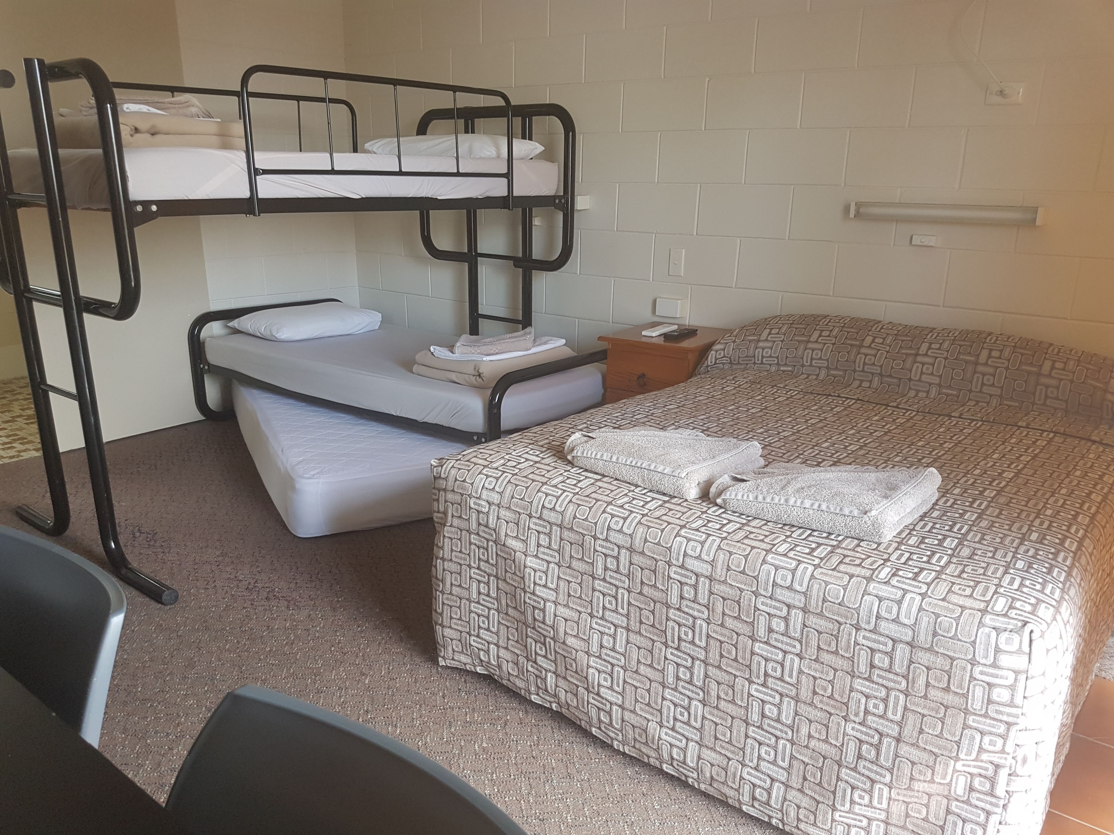 A bunk bed room with a patterned bedspread, a small bedside table, and a chair.
