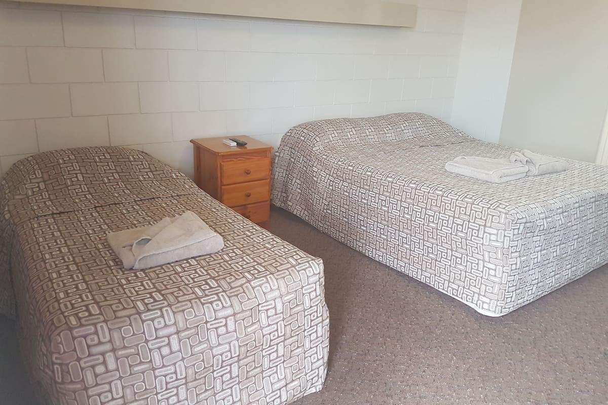 A room with two single beds, a wooden nightstand, and a white brick wall.