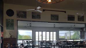 A spacious dining area with multiple tables and chairs, large windows providing natural light, and a ceiling fan. - Monto Colonial Motor Inn (Monto)