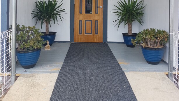 A hotel entrance with a wooden door, a black carpet, potted plants, and directional signs for the office, bar, and restaurant. - Monto Colonial Motor Inn (Monto)