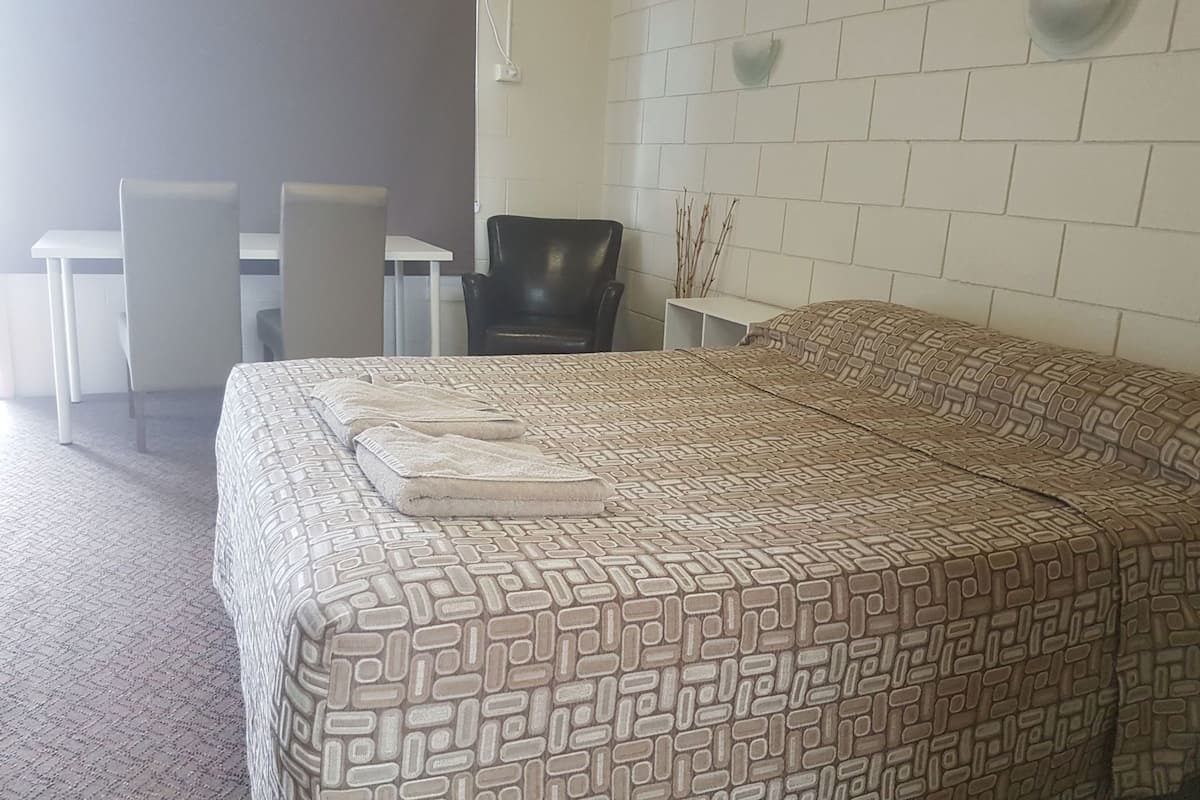 A bedroom with a patterned bedspread, a desk with a chair, and a wall-mounted light fixture.