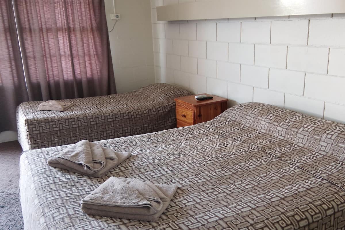 A room with two beds, each with a patterned bedspread and a folded towel. There is a small wooden nightstand between the beds.