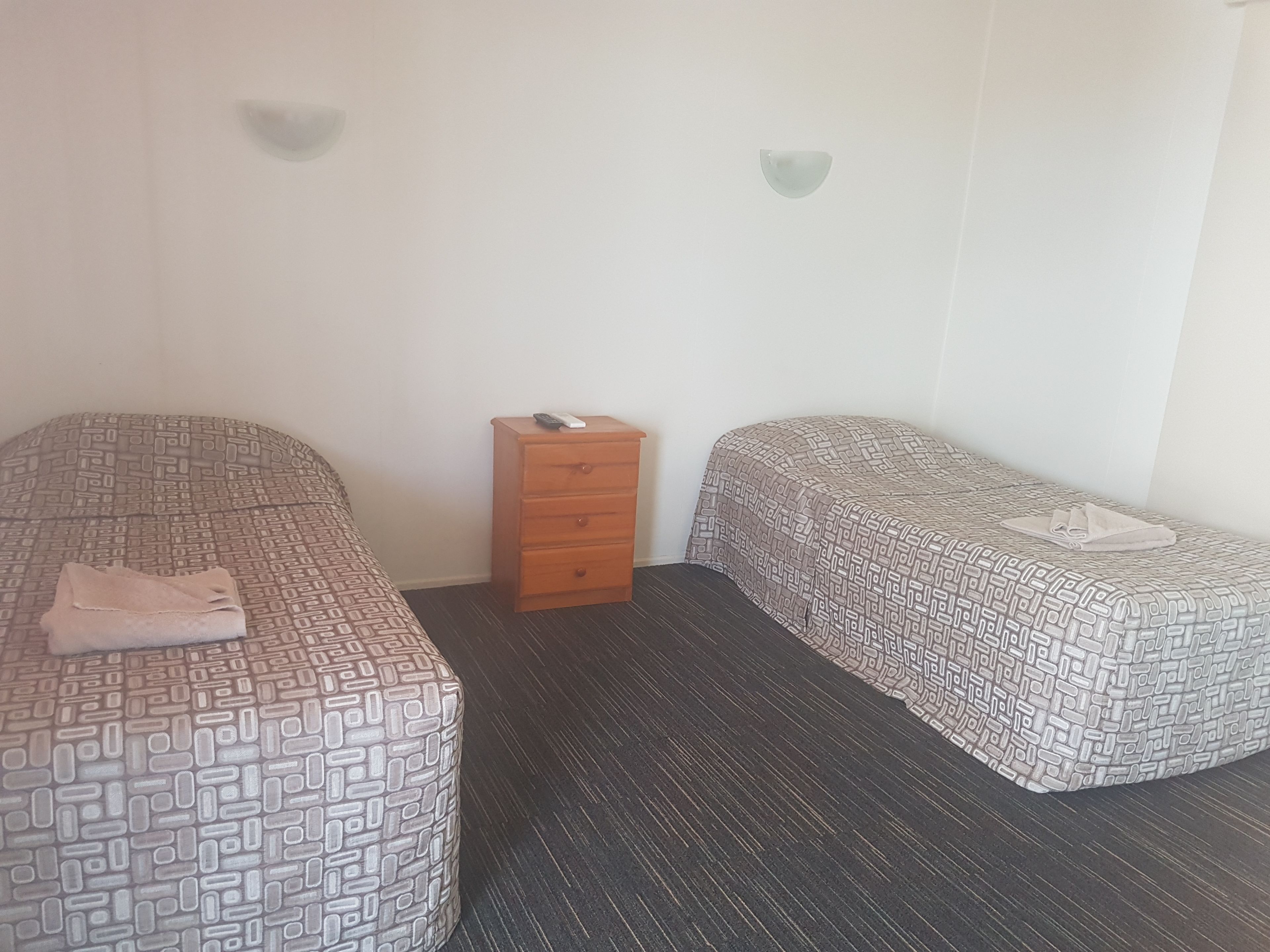 Una habitación con dos camas, una mesita de noche de madera y una lámpara fijada a la pared.