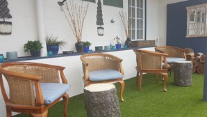A room with three wicker chairs with blue cushions, a stone stump, and a white wall with decorative items. - Monto Colonial Motor Inn (Monto)