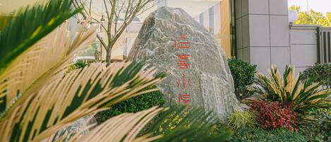 Ein großer Felsen mit chinesischen Schriftzeichen in einem angelegten Garten.
