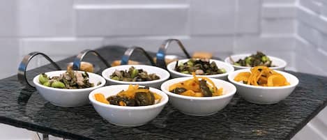 A table with multiple bowls of food, set against a tiled wall.
