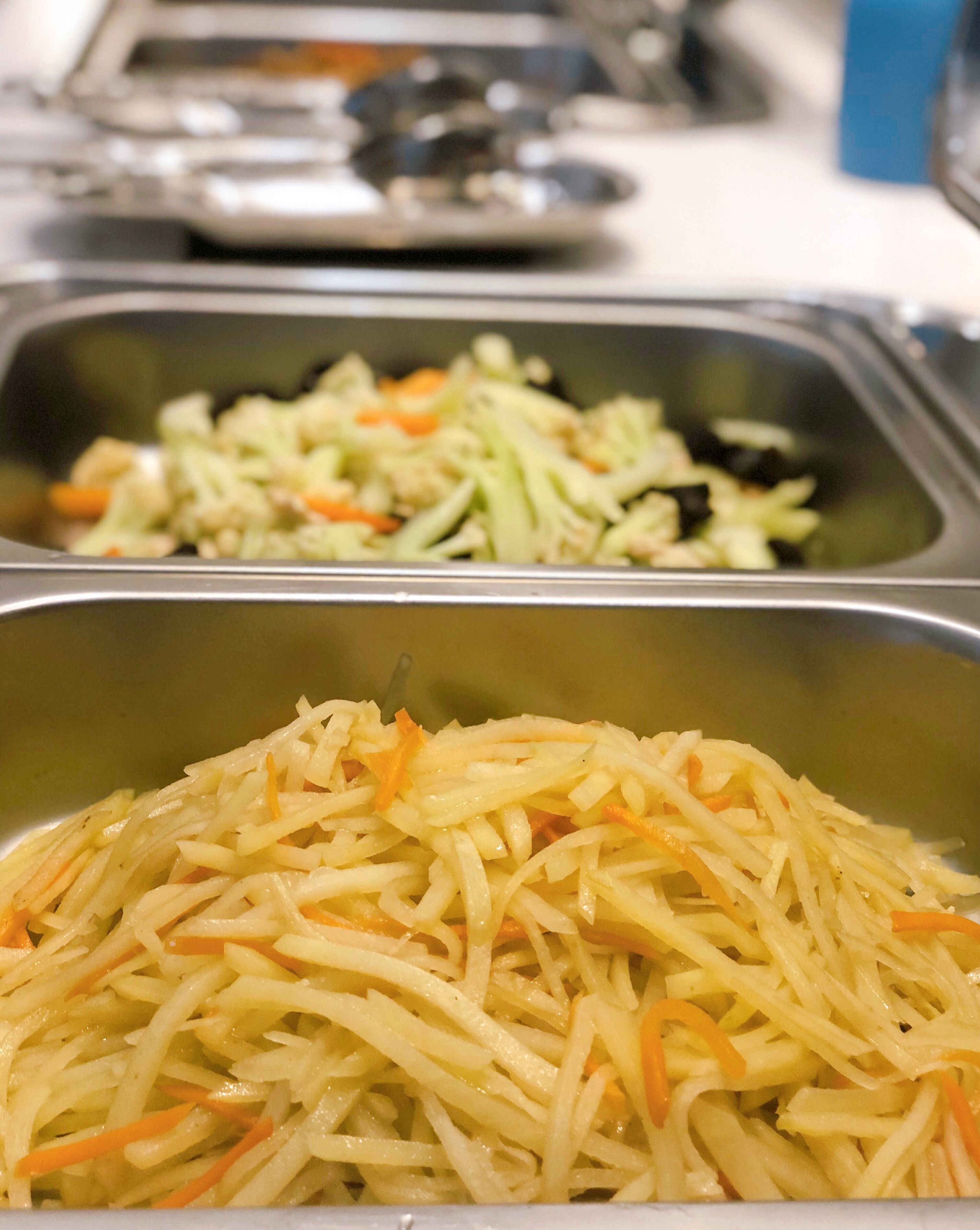 A buffet with two trays of food, one with shredded potatoes and carrots, and the other with a mixed vegetable salad.