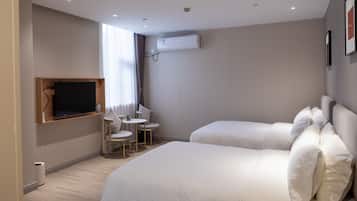 Ein Hotelzimmer mit zwei Betten, einem Wandfernseher, einem kleinen Tisch mit Stühlen und einer Klimaanlage.