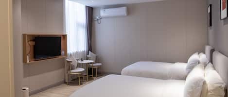 Hotellihuone, jossa on kaksi sänkyä, seinälle asennettu televisio, pieni pöytä tuoleineen ja ilmastointilaite.