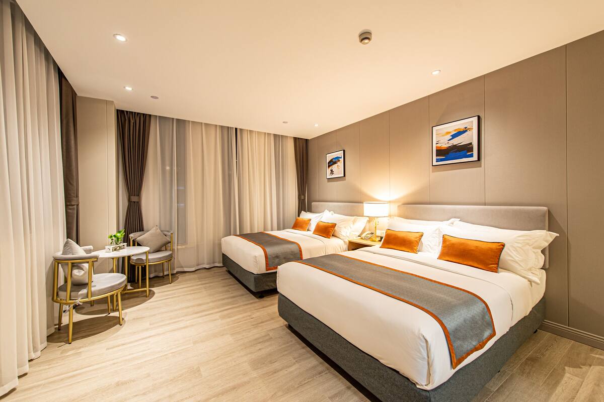 A hotel room with two beds, a small table with chairs, and a window with curtains.