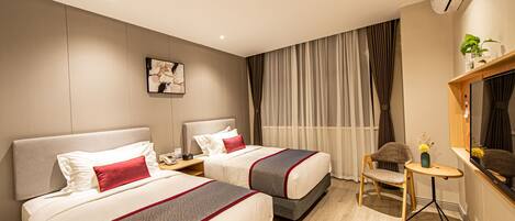 A hotel room with two beds, a small table, a chair, a TV, and a window with curtains.