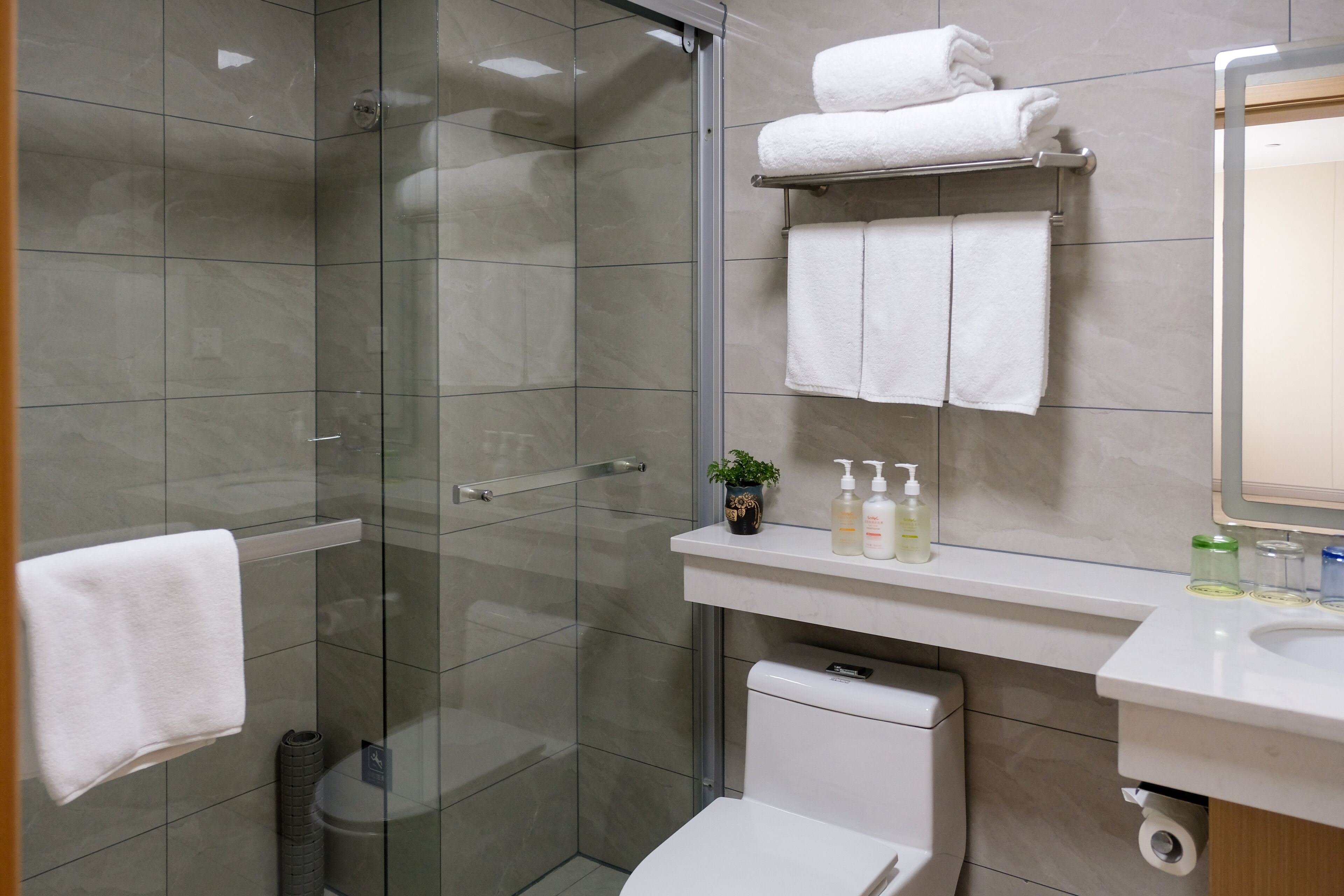 A modern bathroom with a glass shower enclosure, a toilet, a sink, and a towel rack with folded towels.