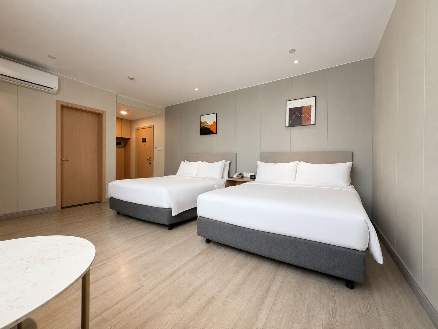 A hotel room with two beds, a desk, and an air conditioning unit.