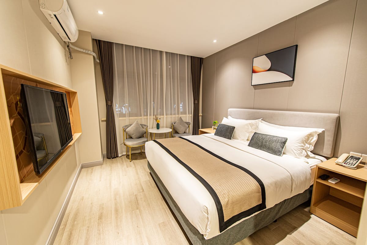 A modern hotel room with a large bed, a flat-screen TV, a small round table, and a bedside table with a phone.