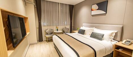 Una habitación de hotel moderna con una cama grande, un televisor de pantalla plana, una pequeña mesa redonda y una mesita de noche con un teléfono.
