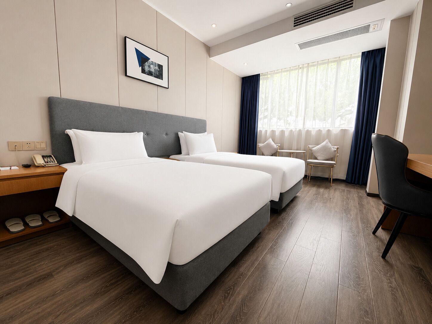 A hotel room with two beds, a desk, a chair, a phone, and a picture on the wall.
