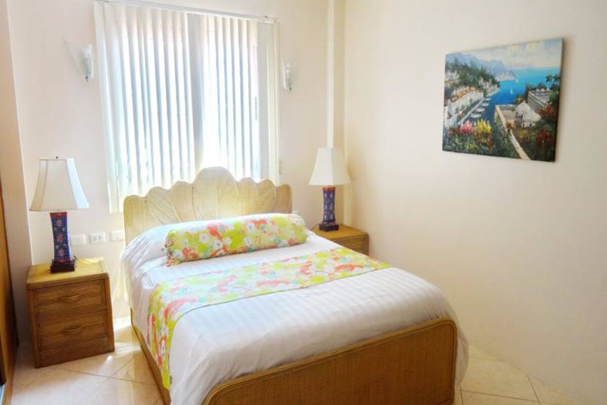 Une chambre à coucher avec un lit, deux lampes de chevet, une fenêtre avec des stores et un tableau au mur.