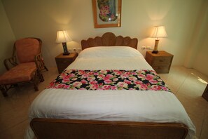 A neatly made bed with a floral bedspread, two bedside lamps, a chair, and a painting on the wall. - Butterfly Garden Boutique Residence by Frasier (Pattaya)