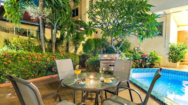A round table with chairs and a poolside setting with a grill and plants. - Butterfly Garden Boutique Residence by Frasier (Pattaya)