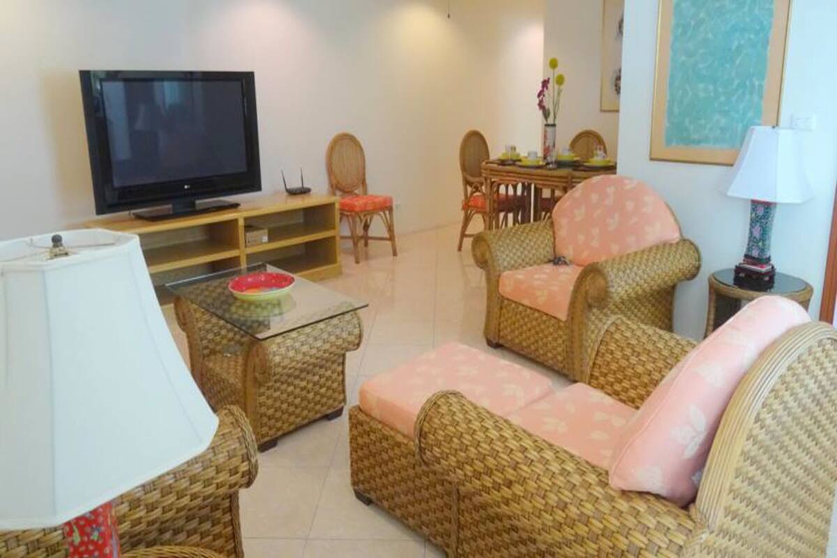 A living room with wicker furniture, a flat-screen TV, a dining table with chairs, and a lamp.