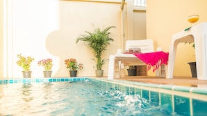 A swimming pool with a white chair and a pink towel, surrounded by potted plants. - Butterfly Garden Boutique Residence by Frasier (Pattaya)