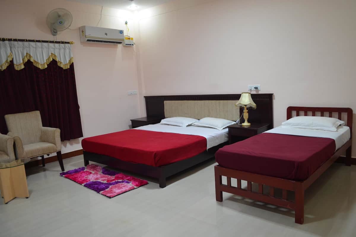 A hotel room with two single beds, a chair, a small table, a fan, and an air conditioning unit.