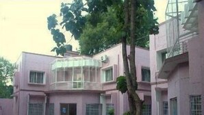 A building with a pink exterior, a central courtyard with a tree, and a checkered pavement. - KSTDC Hotel Mayura Chalukya Badami (Badami)