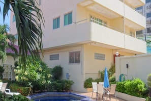 A two-story building with a balcony on the upper floor, a small pool, and outdoor seating.