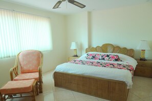 A bedroom with a bed, a chair, a nightstand, a lamp, and a ceiling fan.