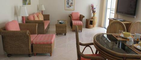 Una sala de estar con mobiliario de mimbre, una mesa con cubierta de vidrio y un televisor.