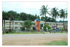 A building with a prominent orange section, surrounded by greenery and palm trees. - KSTDC Hotel Mayura Vijayanagara (Hospet)