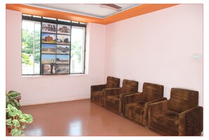 A room with a large window, a wall-mounted shelf with photos, and three brown armchairs. - KSTDC Hotel Mayura Vijayanagara (Hospet)