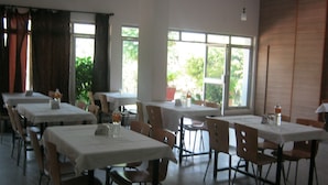 Un comedor con mesas y sillas, ventanas amplias con vistas a follaje y un ventilador de techo.
