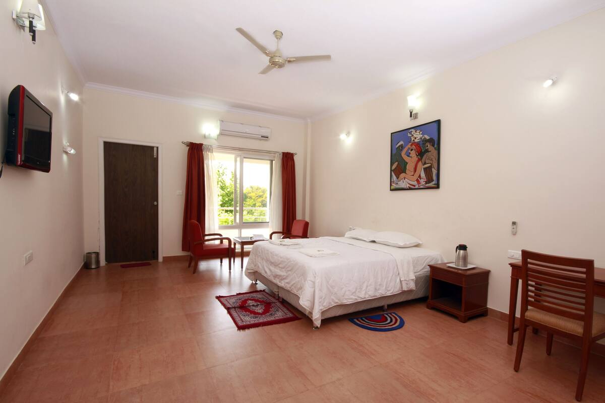 A bedroom with a bed, a desk, a chair, a TV, a ceiling fan, and a window with curtains.