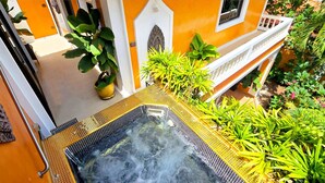 A hot tub with a metal safety railing, surrounded by lush green plants and a yellow building with a white door and window. - HIDELAND Luxury Pool Villa Pattaya Walking Street (Pattaya)