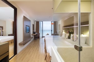 Habitación de hotel moderna con cama, escritorio y zona de estar, que cuenta con un ventanal con vistas al mar.