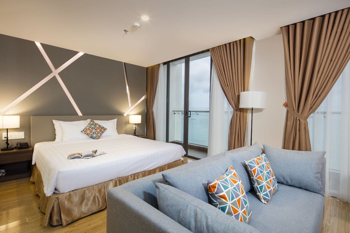 A modern hotel room with a large bed, a sofa, and a balcony with curtains.