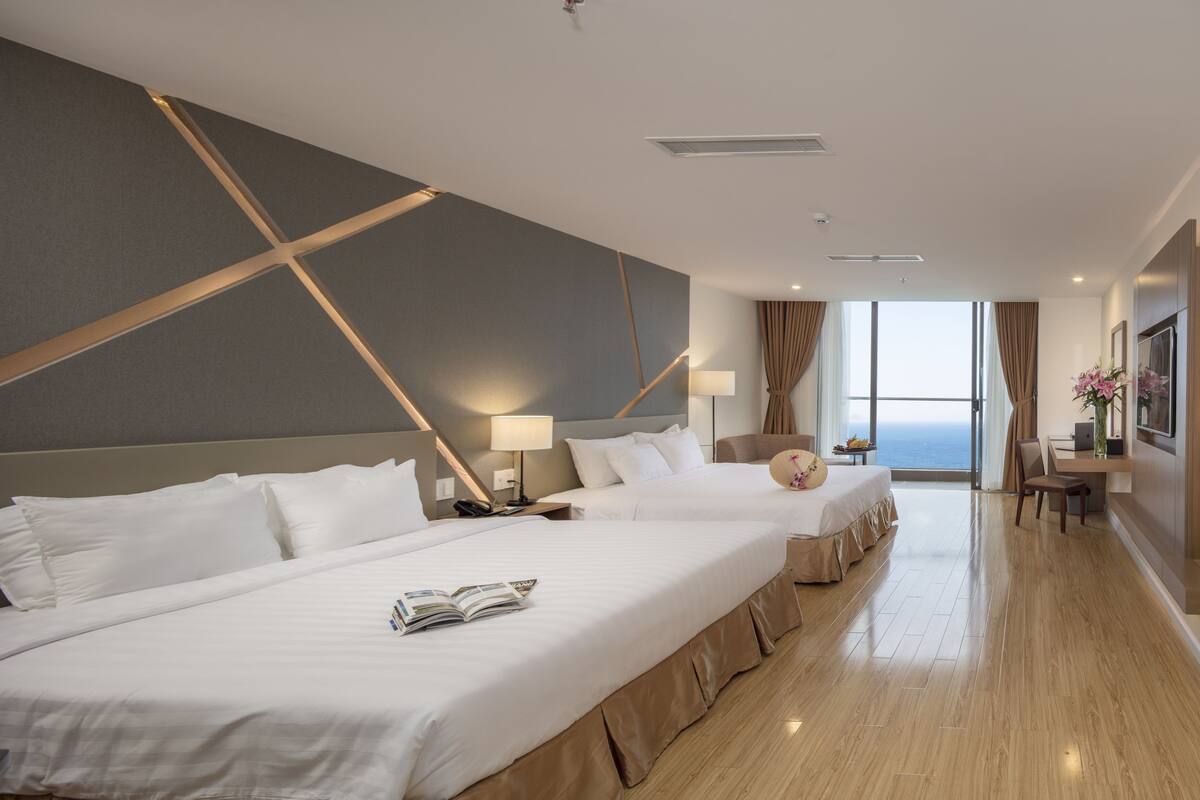 A hotel room with two beds, a desk, a chair, a TV, and a large window with a view.